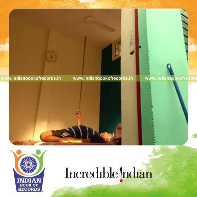 individual balancing cue stick on index finger while holding reclined thunderbolt pose for record in Indian Book of Records