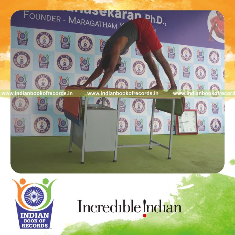 individual holding adho mukha svanasana yoga pose blindfolded on a table for record in Indian Book of Records