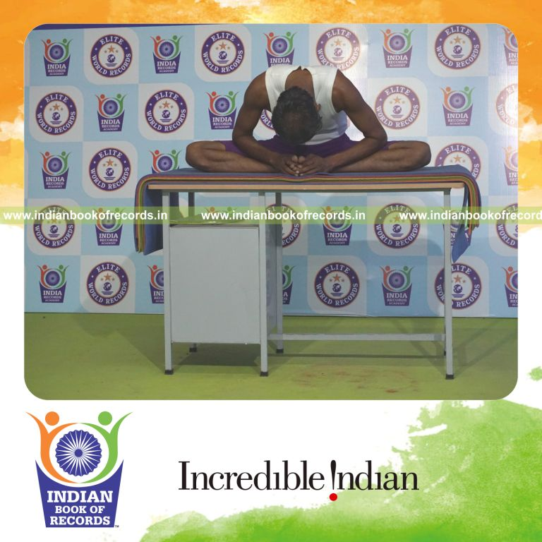 individual holding baddha konasana yoga pose blindfolded on a table for record in Indian Book of Records