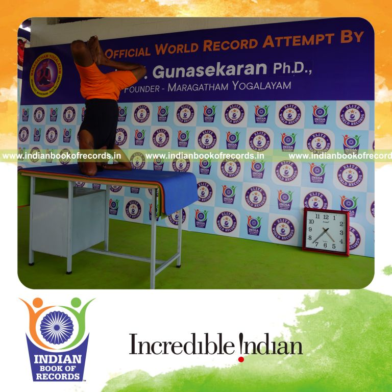 individual holding baddha sirasasana yoga pose blindfolded on a table for record in Indian Book of Records