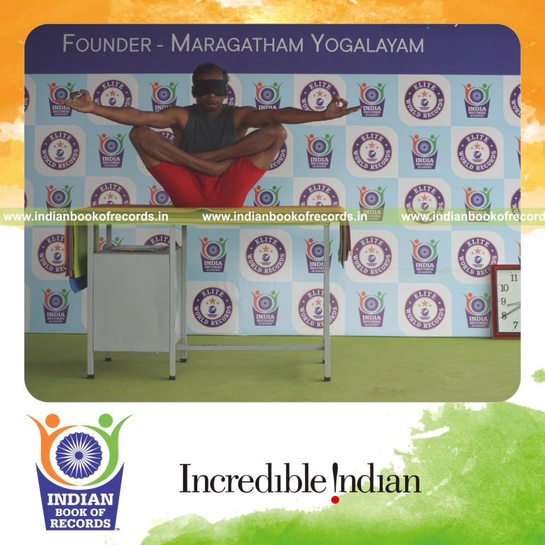 individual holding chinmudra thulangasana yoga pose blindfolded on a table for record in Indian Book of Records