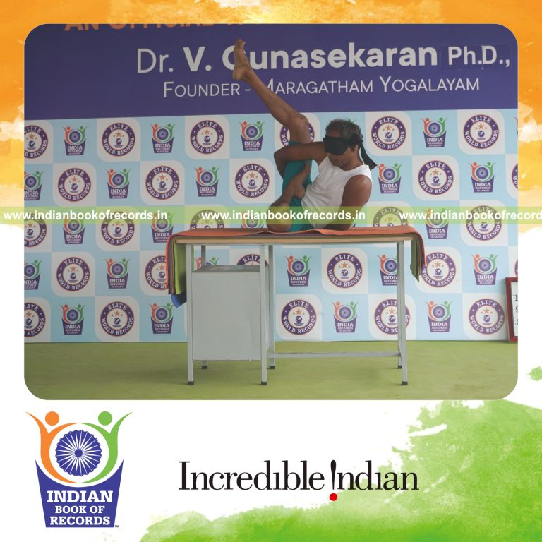 individual holding daksina ardha baddha parsva krounchasana yoga pose blindfolded on a table for record in Indian Book of Records