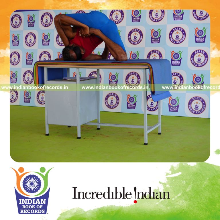 individual holding daksina ardha padma astavakrasana yoga pose blindfolded on a table for record in Indian Book of Records