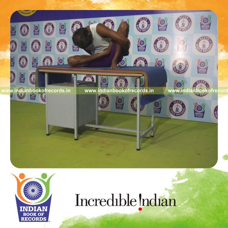 individual holding daksina ardha padma marichyasana yoga pose blindfolded on a table for record in Indian Book of Records