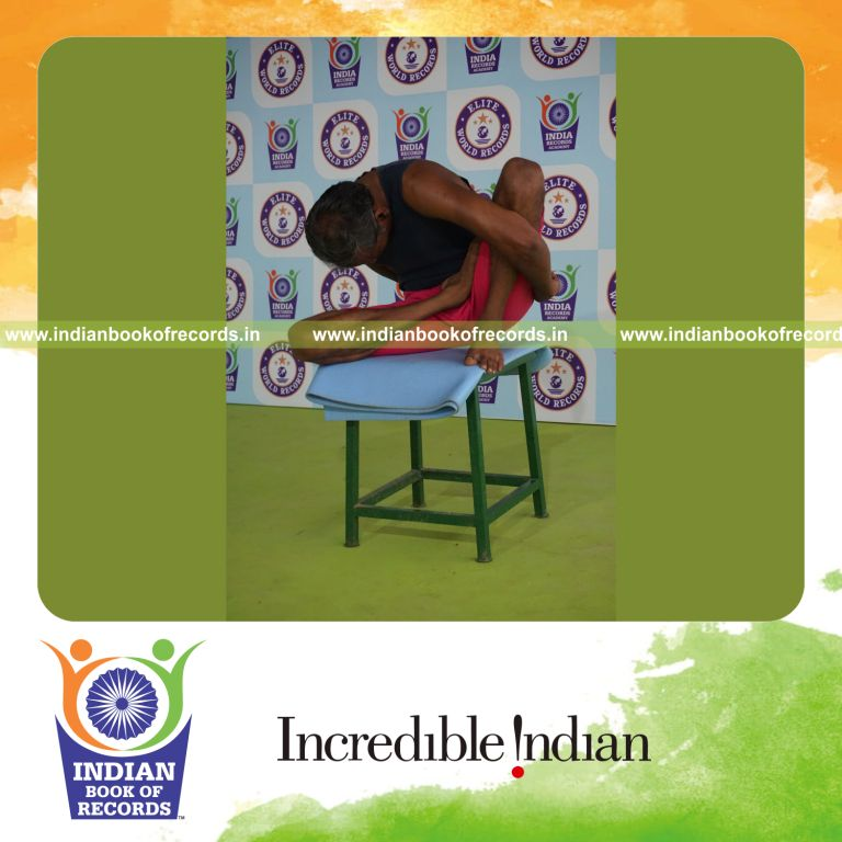 individual holding daksina ardha padma marichyasana yoga pose on a stool for record in Indian Book of Records