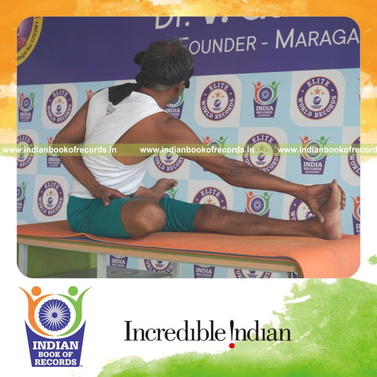 individual holding daksina ardha padma matsyendrasana yoga pose blindfolded on a table for record in Indian Book of Records
