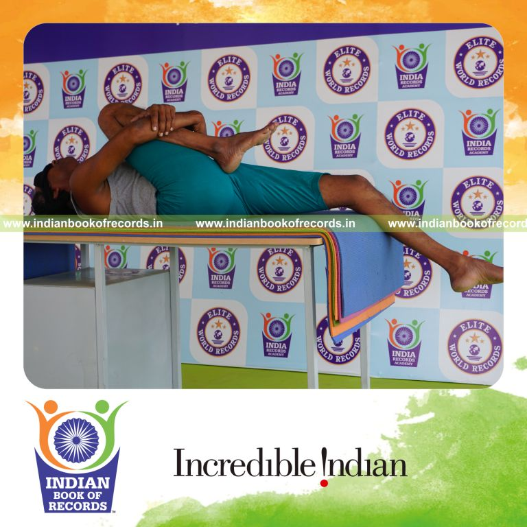 individual holding daksina ardha pavanamuktasana yoga pose blindfolded on a table for record in Indian Book of Records