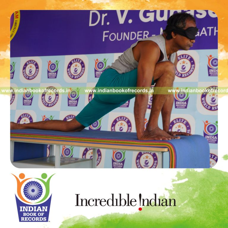 individual holding daksina asva chanjalanasana yoga pose blindfolded on a table for record in Indian Book of Records