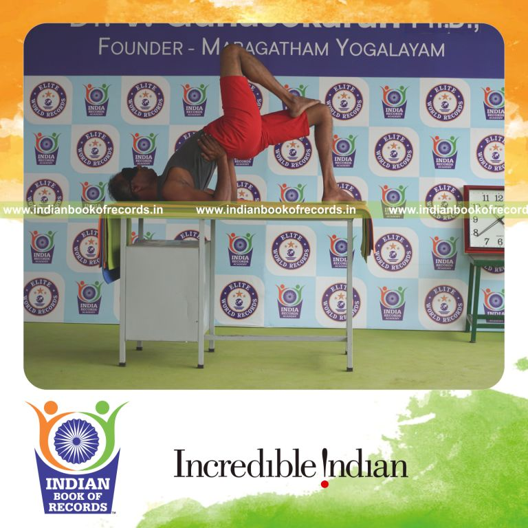 individual holding daksina ekapada janu setu bandha sarvangasana yoga pose blindfolded on a table for record in Indian Book of Records