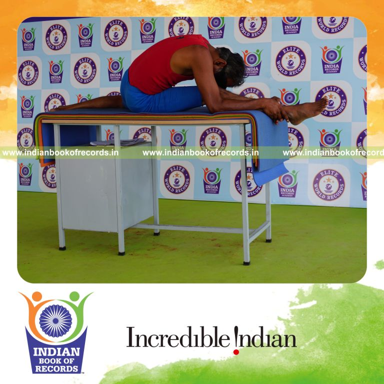 individual holding daksina hanumana paschimottanasana yoga pose blindfolded on a table for record in Indian Book of Records