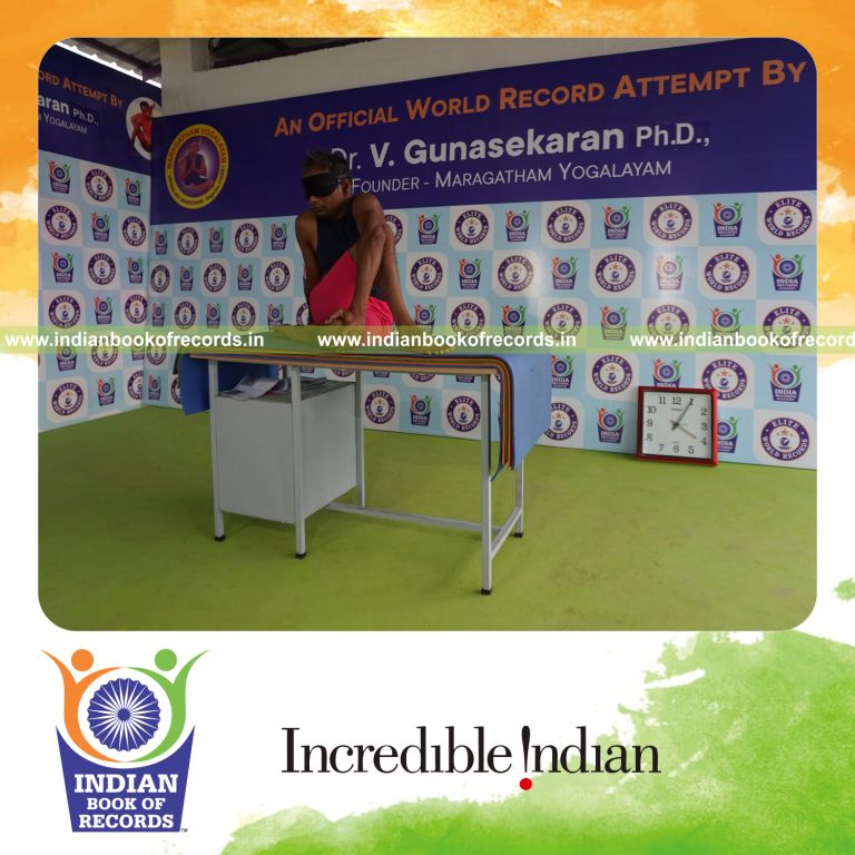 individual holding daksina janu ardha matsyendrasana yoga pose blindfolded on a table for record in Indian Book of Records