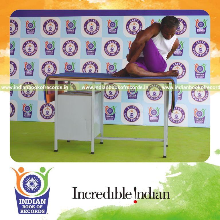 individual holding daksina janu parivrtta ardha matsyendrasana yoga pose on a table for record in Indian Book of Records
