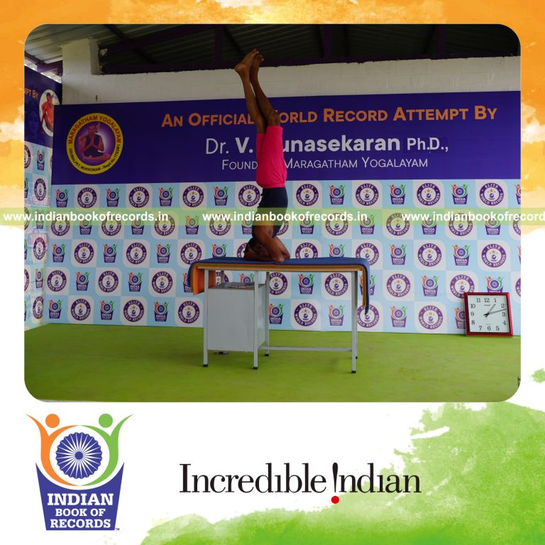 individual holding daksina parivrtaikapata sirsasana yoga pose on a table for record in Indian Book of Records
