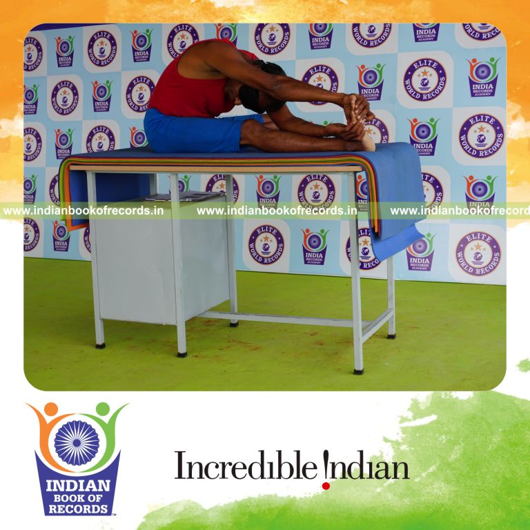 individual holding daksina parivrtana janu sirsasana yoga pose blindfolded on a table for record in Indian Book of Records