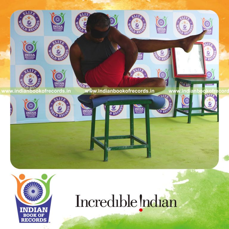 individual holding daksina parivrtta ardha matsyendrasana yoga pose blindfolded on a stool for record in Indian Book of Records