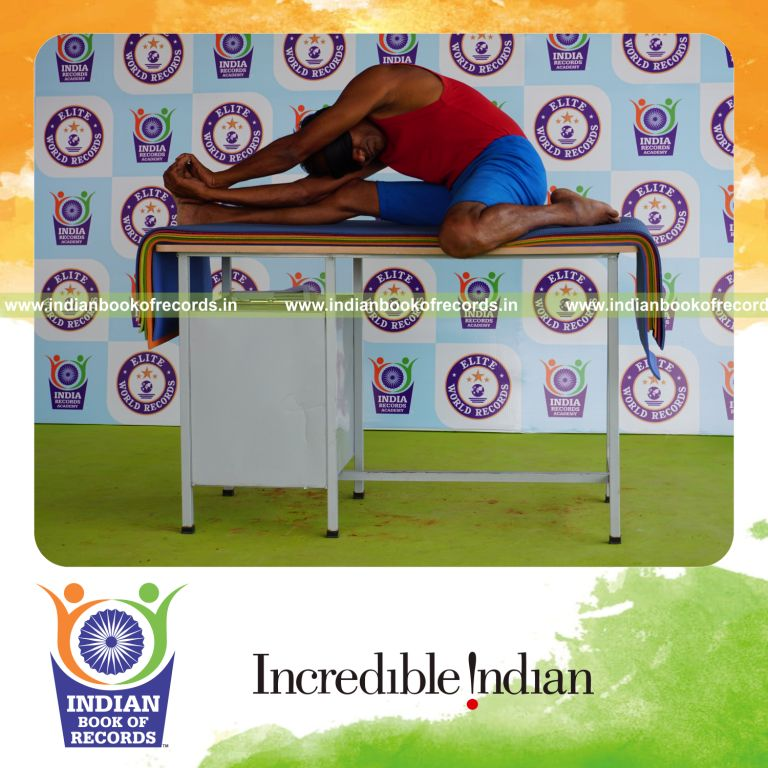 individual holding daksina parivrtta gomukha janu sirsasana yoga pose blindfolded on a table for record in Indian Book of Records