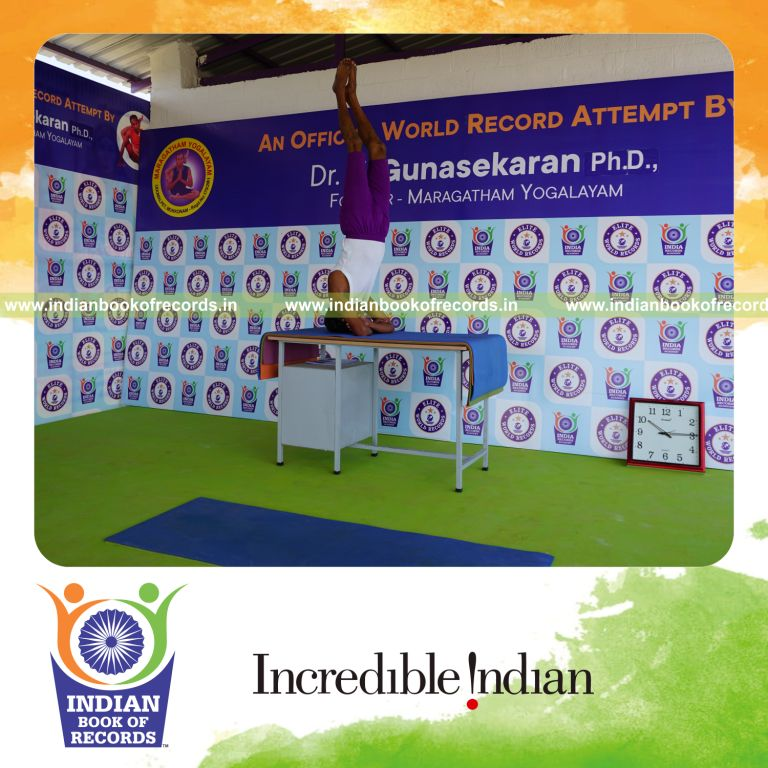individual holding daksina parsva baddha hastha sirsasana yoga pose blindfolded on table for record in Indian Book of Records