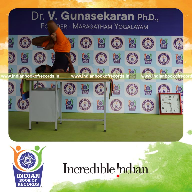 individual holding daksina parsva padma sarvangasana yoga pose blindfolded on a table for record in Indian Book of Records