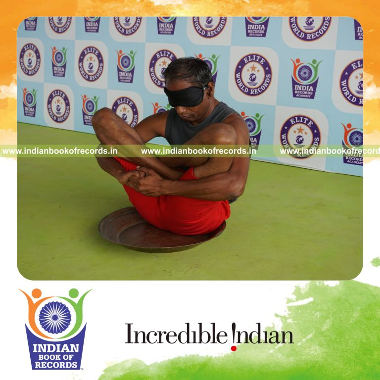 individual holding garbha pindasana yoga pose blindfolded on a brass plate for record in Indian Book of Records
