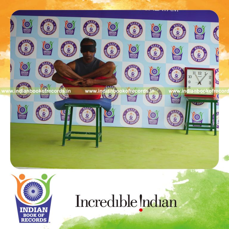 individual holding garbha pindasana yoga pose blindfolded on a stool for record in Indian Book of Records