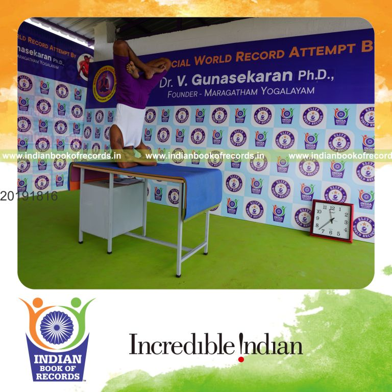 individual holding padma baddha hastha sirsasana yoga pose blindfolded on a table for record in Indian Book of Records