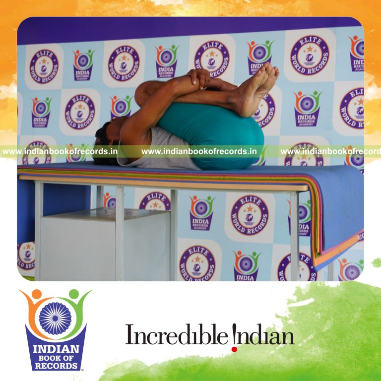 individual holding pavanamuktasana yoga pose blindfolded on a table for record in Indian Book of Records