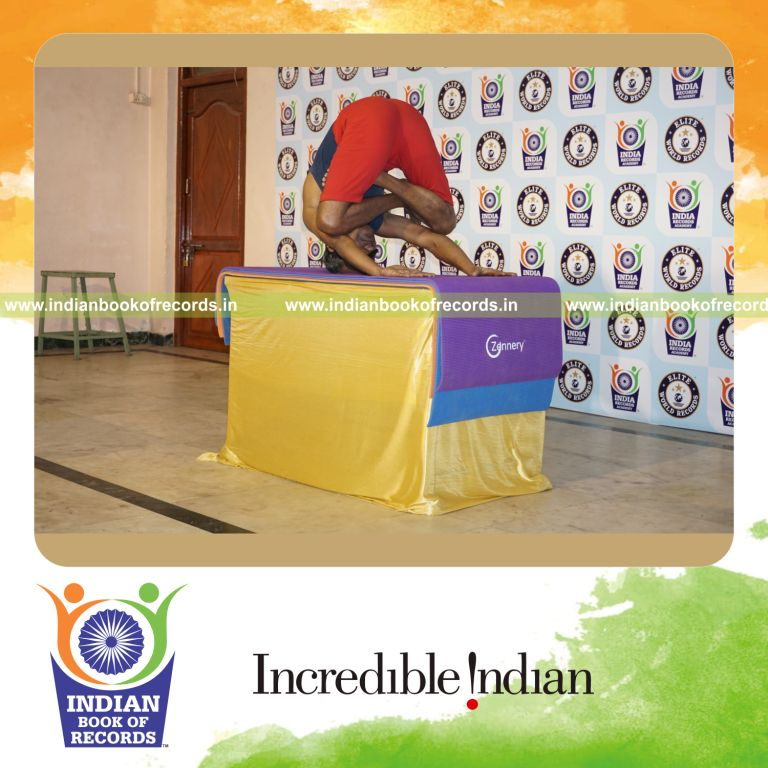 individual holding pindasana in mukta sirsasana yoga pose blindfolded on a table for record in Indian Book of Records