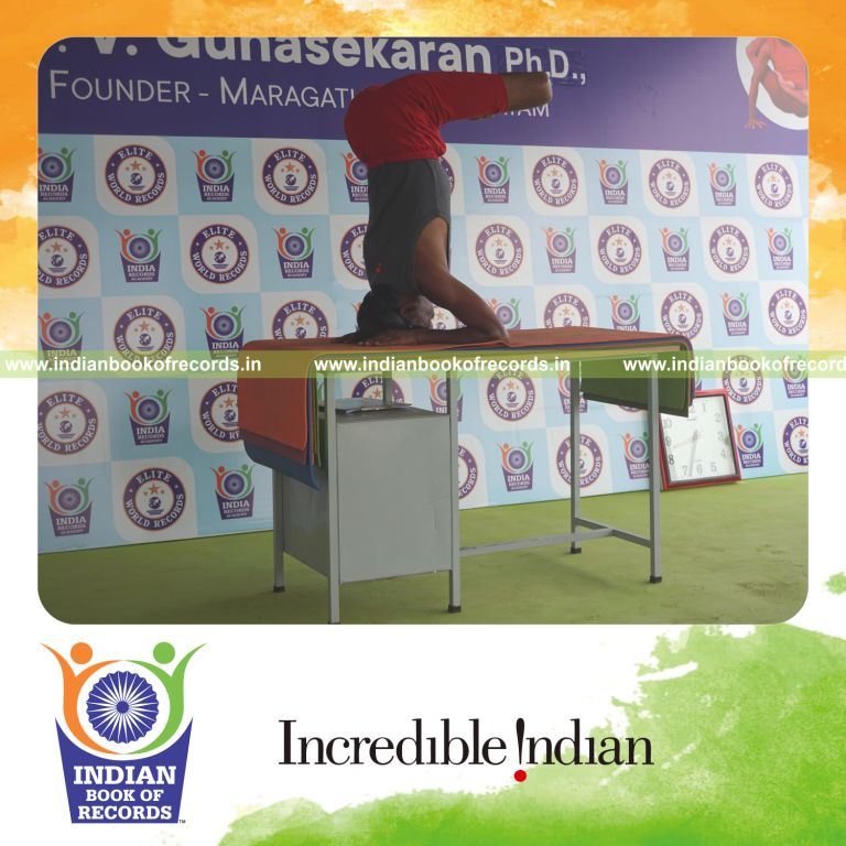 individual holding pindasana in salamba sirsasana yoga pose blindfolded on a table for record in Indian Book of Records