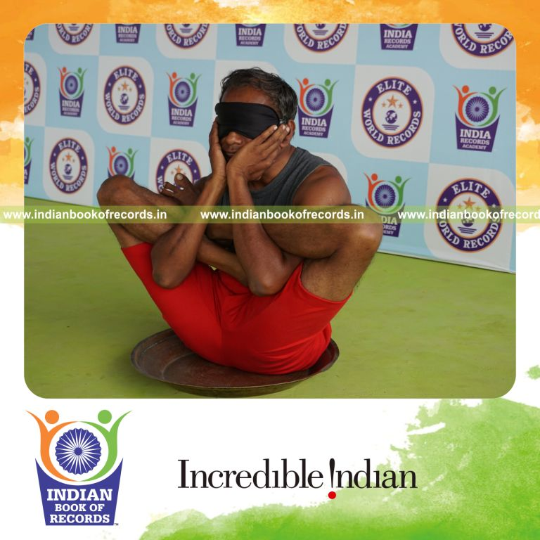 individual holding purna garbha pindasana yoga pose blindfolded on a brass plate for record in Indian Book of Records