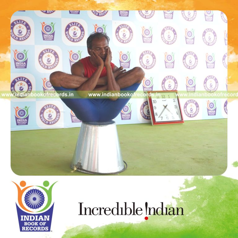 individual holding purna garbha pindasana yoga pose on a bucket for record in Indian Book of Records