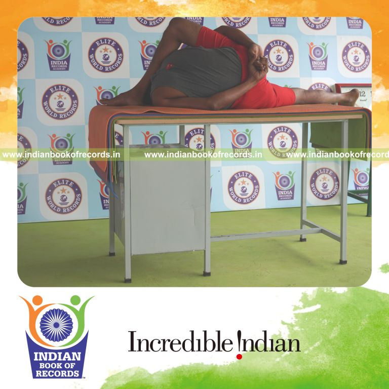 individual holding vama ardha astavakrasana yoga pose blindfolded on a table for record in Indian Book of Records