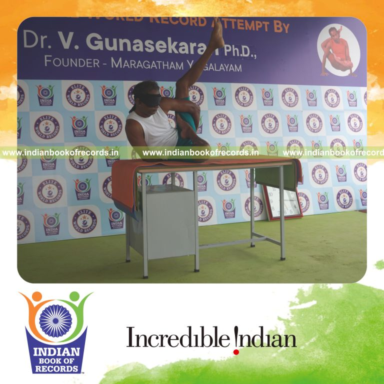 individual holding vama ardha baddha parsva krounchasana yoga pose blindfolded on a table for record in Indian Book of Records