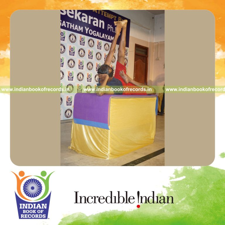 individual holding vama ardha padma anantasana yoga pose blindfolded on a table for record in Indian Book of Records