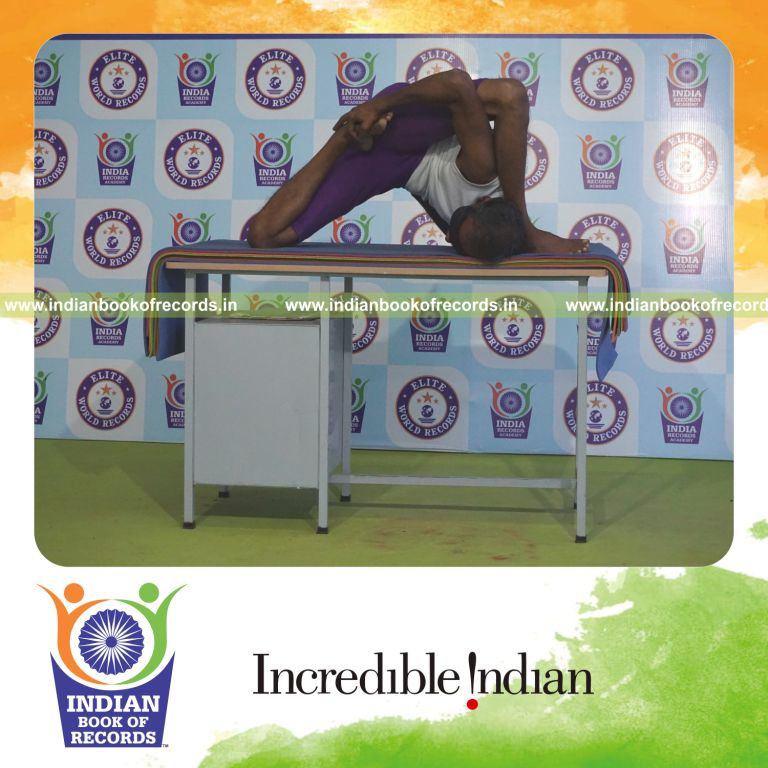 individual holding vama ardha padma astavakrasana yoga pose blindfolded on a table for record in Indian Book of Records