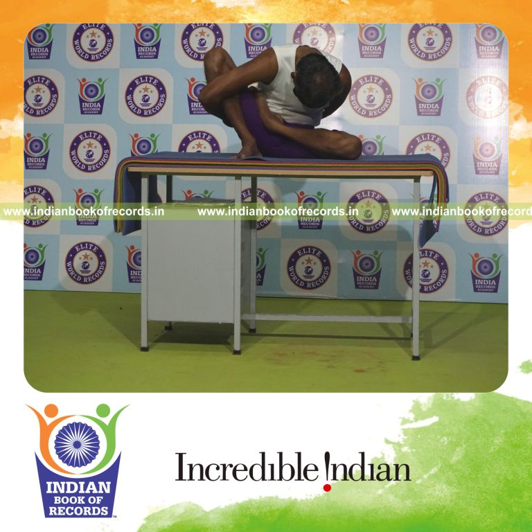 individual holding vama ardha padma marichyasana yoga pose blindfolded on a table for record in Indian Book of Records