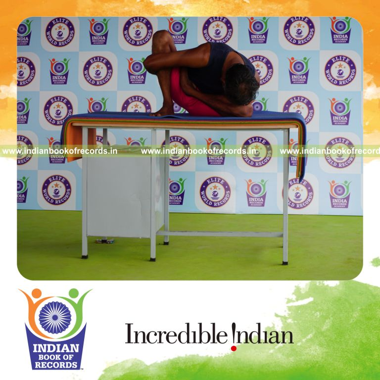 individual holding vama ardha padma marichyasana yoga pose on a table for record in Indian Book of Records