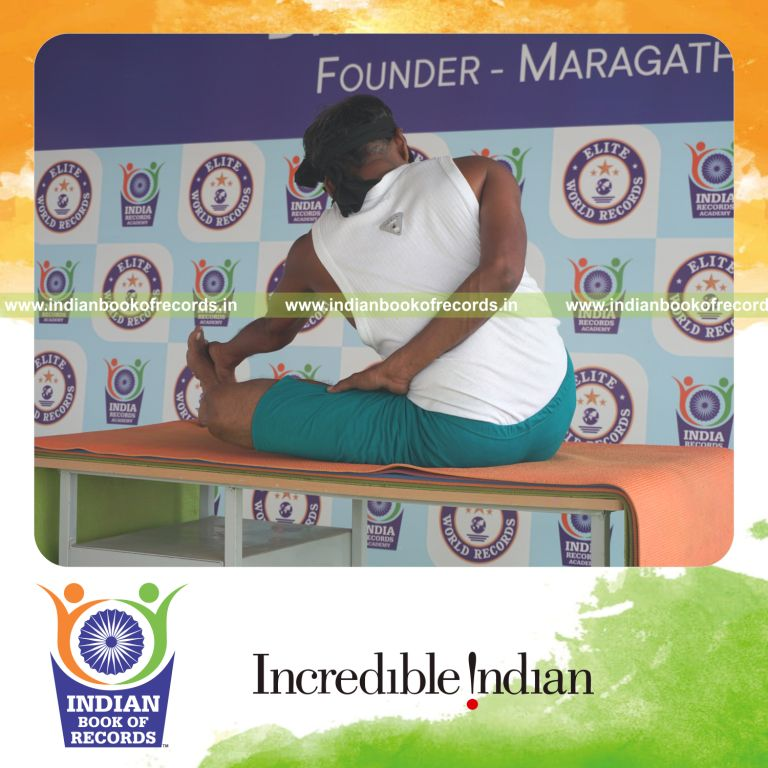 individual holding vama ardha padma matsyendrasana yoga pose blindfolded on a table for record in Indian Book of Records