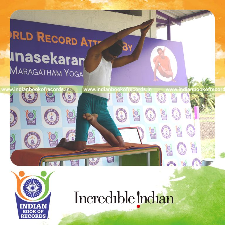 individual holding vama ardha padma ustraa konasana yoga pose blindfolded on a table for record in Indian Book of Records