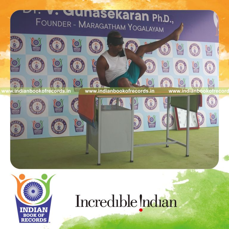 individual holding vama ardha parsva krounchasana yoga pose blindfolded on a table for record in Indian Book of Records