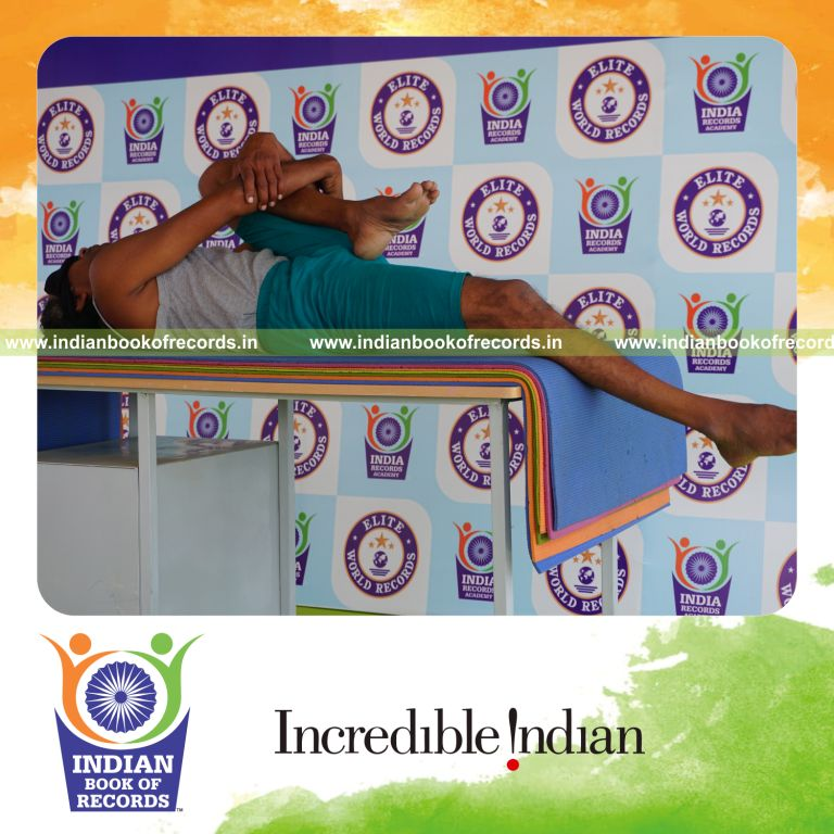 individual holding vama ardha pavanamuktasana yoga pose blindfolded on a table for record in Indian Book of Records