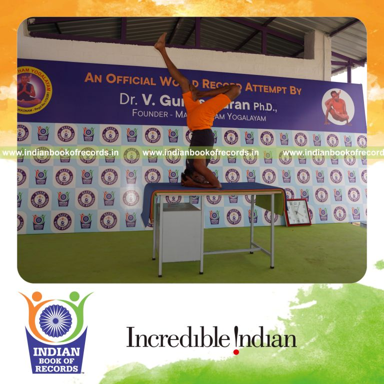 individual holding vama ardha sirsasana yoga pose blindfolded on a table for record in Indian Book of Records