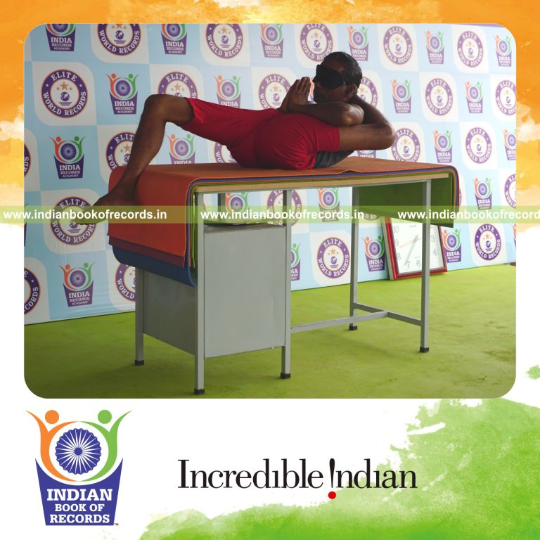 individual holding vama bhairavasana yoga pose blindfolded on a table for record in Indian Book of Records