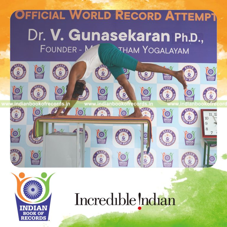 an individual holding vama ekapada adho mukha svanasana yoga pose blindfolded on a table continuously for the longest duration with stability and control for a record in Indian Book of Records
