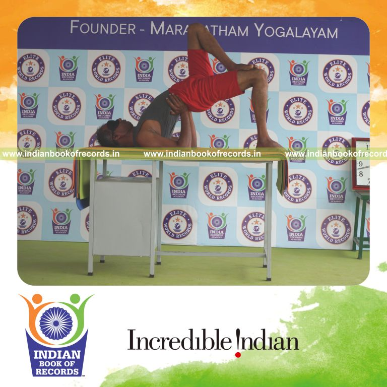 individual holding vama ekapada janu setu bandha sarvangasana yoga pose blindfolded on a table for record in Indian Book of Records