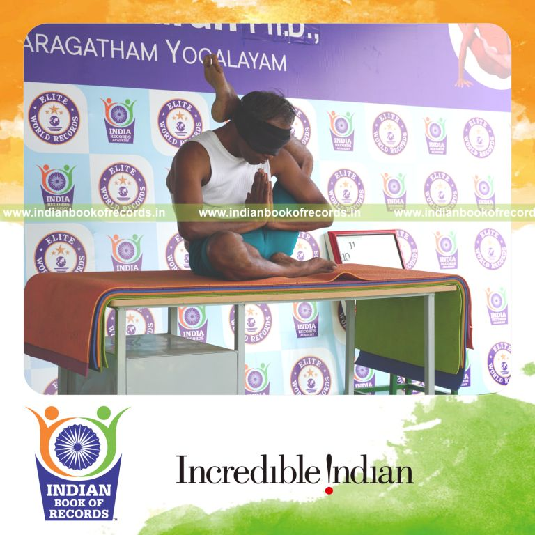individual holding vama ekapada sirsasana yoga pose blindfolded on a table for record in Indian Book of Records