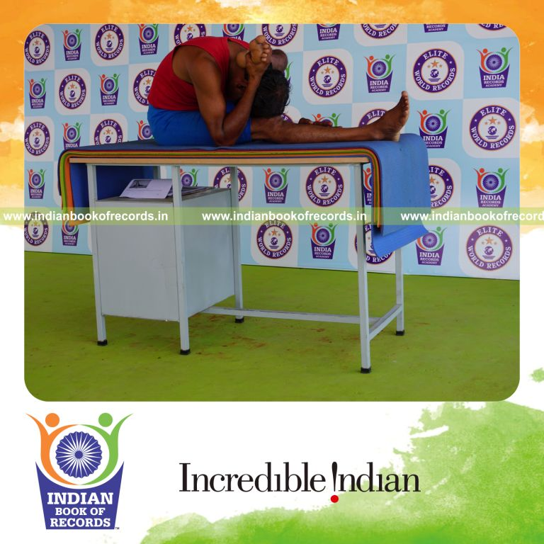 individual holding vama ekapada skandasana yoga pose blindfolded on a table for record in Indian Book of Records