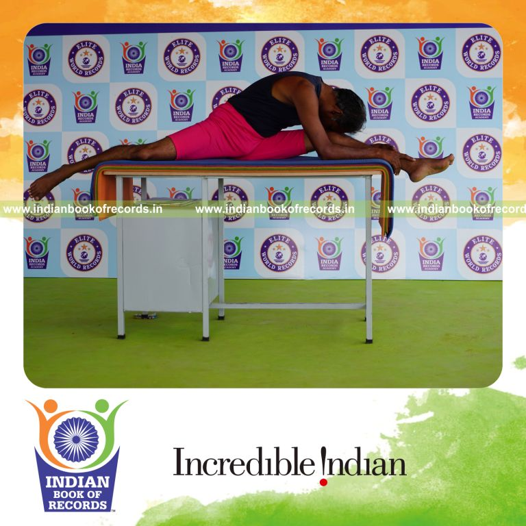 individual holding vama hanumana paschimottanasana yoga pose on a table for record in Indian Book of Records
