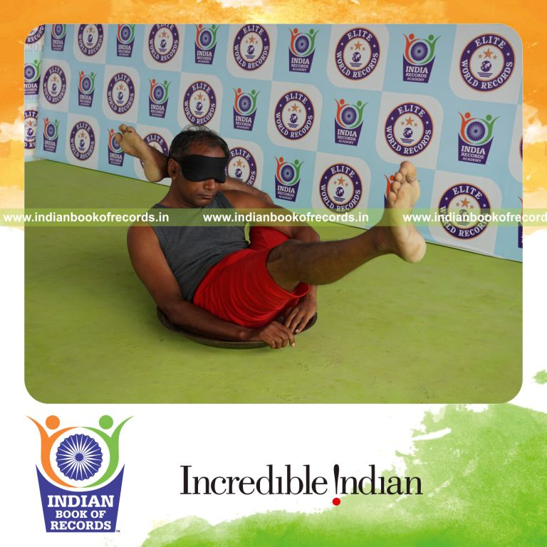 individual holding vama kala bhairavasana yoga pose blindfolded on a brass plate for record in Indian Book of Records