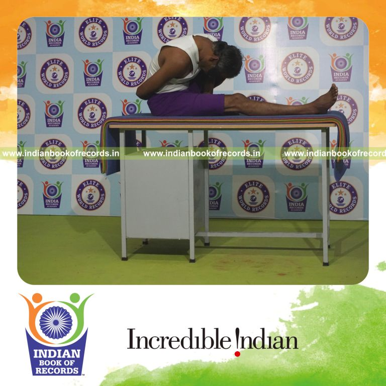 individual holding vama marichyasana yoga pose blindfolded on a table for record in Indian Book of Records