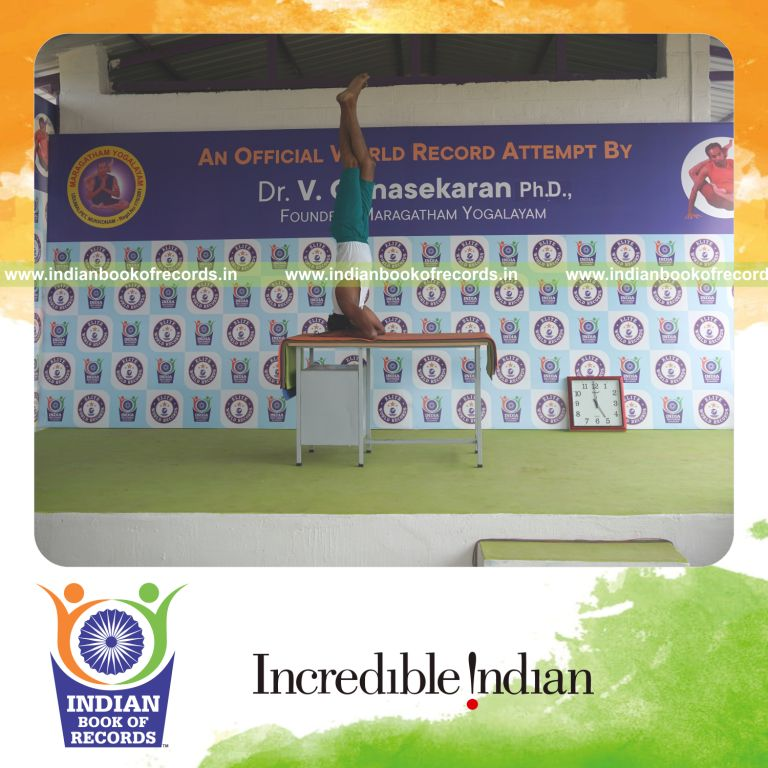 individual holding vama parivrtaikapata salamba sirsasana yoga pose blindfolded on a table for record in Indian Book of Records